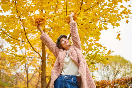 Portrait of an amusing young woman enjoying a nice autumn day in a beautiful picturesque park holding a bouquet of yellow maple leaves. Happy autumn mood.の写真素材