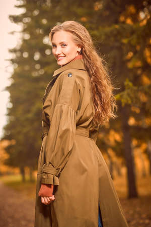 Portrait of a pretty young woman walking in a beautiful autumn park happily smiling. Joyful autumn mood.の写真素材