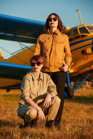 Full length portrait of two beautiful professional female commercial aviation pilots in uniform and sunglasses posing in the background of their plane. Aviation.の写真素材