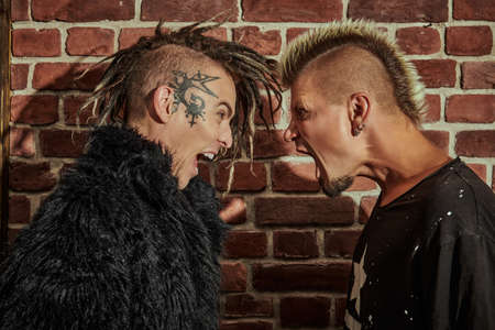 Two punk rock musicians in concert costumes stand face to face screaming at each other in the background of a brick wall. Youth alternative culture. Grunge style.の写真素材