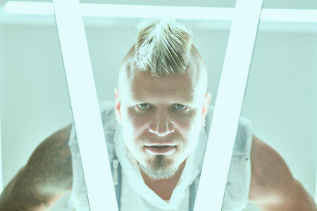 Cool attractive punk rock musician man with mohawk and beard poses at the studio among neon lights....