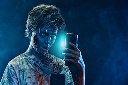 Halloween. Scary zombie boy teenager makes selfie on his smartphone. Copy space.の写真素材