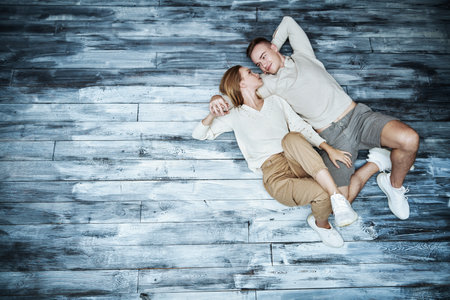 Happy carefree lovers. Happy young pair lie on a loft style  floor looking at each other with love and holding hands. Copy space.の写真素材