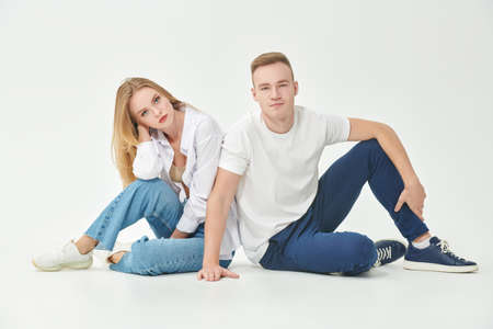 Studio portrait of a beautiful enamored girl and guy pose sitting next to each other. Full length portrait on a white background. Love concept.の写真素材