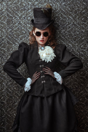 Portrait of an elegant woman in traditional 19th century clothes and stylish sunglasses posing on a vintage background. Style of the late 19th - early 20th century.の写真素材