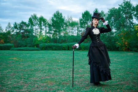 Full length portrait of a stunning  young lady in a strict black suit of the 19th century posing in an autumn park.の写真素材