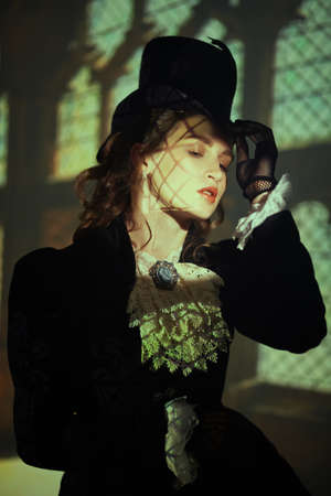 Fashion of the late 19th - early 20th century. Portrait of an elegant lady in a black dress and hat on the background of the railway station. Steampunk lady.の写真素材