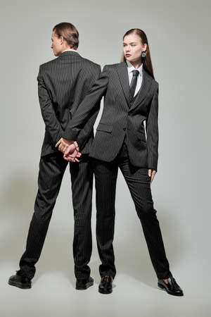 Full length portrait of a stylish couple of young people man and woman in elegant striped pantsuits on a gray background. Impeccable look. Men's clothing style. Fashion shoot.の写真素材