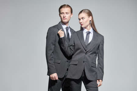 Fashion shoot. Stylish couple of young people man and woman in elegant striped pantsuits. Studio portrait on a gray background. Impeccable look. Men's clothing style.の写真素材