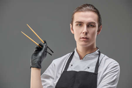 Japanese food. Portrait of a male chef holding Japanese chopsticks on a gray background. Studio shot.の写真素材