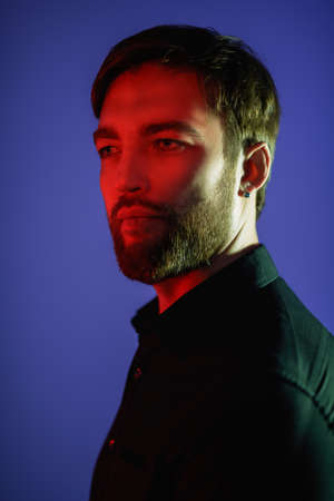 Portrait of a handsome serious middle-aged man in classic suit posing in a blue studio background with red light on his face. Businessman portrait. Men's fashion.の写真素材