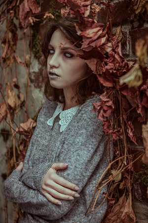 A sad ghost girl with faded eyes and matted black hair stands lonely among withered foliage. Horror film, thriller. Halloween.の写真素材