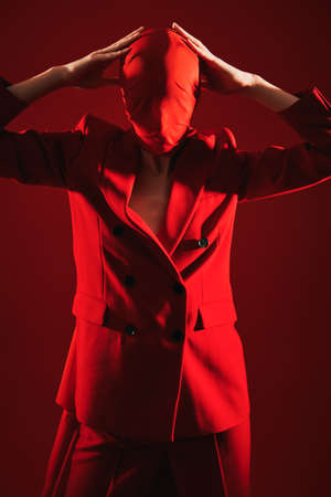 Art and fashion. High fashion female model poses in red suit and red chiffon fabric on the head. Studio portrait on a red background.の写真素材