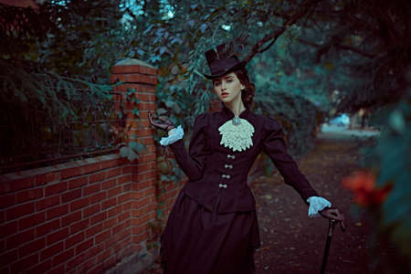 Portrait of a beautiful brunette lady with makeup, hairstyle and clothes of the 19th century walking along a quiet evening street. Historical hairstyle and makeup.の写真素材