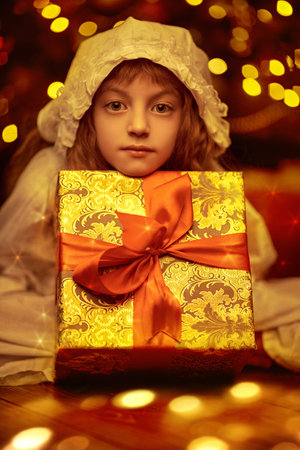 Christmas fairy tales. A cute little girl in a nightgown and a cap poses with a box of present lying...