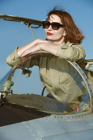 Commercial and military aviation. Beautiful happy woman pilot dressed in uniform and sunglasses poses in her aircraft cockpit ready for take off.の写真素材