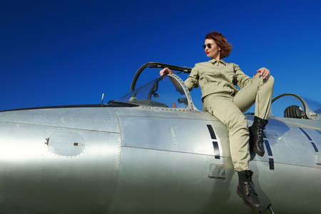 Military and commercial aircraft. Full length portrait of a confident pilot woman wearing uniform and sunglasses posing on her fighter jet ready to fly.の写真素材