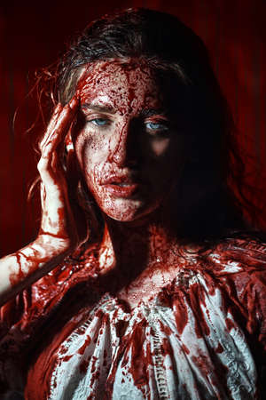 Portrait of a poor innocent girl drenched in blood standing weak in a dark gloomy castle. Horror, thriller. Halloween. Vampires.の写真素材