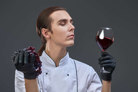 Portrait of a professional sophisticated young male shef  looking at a glass of excellent red wine in his hand.の写真素材
