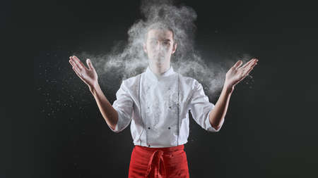 Professional male pastry chef prepares an exquisite dish with flour flying in the air in a restaurant kitchen. Food and meals.の写真素材
