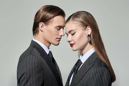 Stylish young couple in smart striped pantsuits poses on a gray studio background. Impeccable look. Business style. Fashion shot.の写真素材