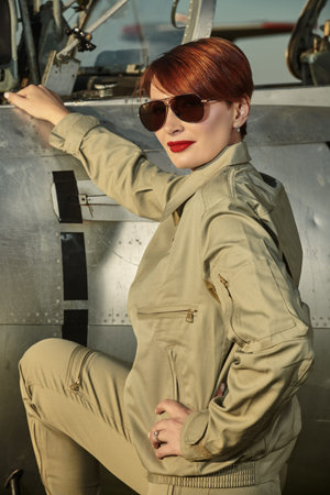 Military and commercial aircraft. Portrait of a confident pilot woman wearing uniform and sunglasses posing next to her fighter jet.の写真素材