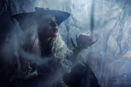 Halloween. Portrait of a evil dark  witch holding out a poisoned apple in  dark forest.の写真素材