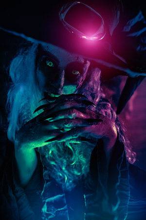 Portrait of a terrifying ugly witch in black garment and hat in an abandoned witch's den. Halloween. Scary tales.の写真素材