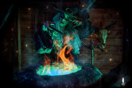 Horrible old witch brews potion in her cauldron with a magic wand  surrounded by magical coloured lights. Halloween. Scary tales.の写真素材