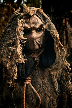 A portrait of an evil Scarecrow with a canvas bag on his head and in a burlap robe, standing in a deep forest. Vintage style. Halloween Tales. Horror, thriller.の写真素材