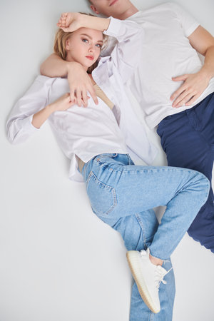 Happy carefree lovers. Beautiful young pair spending their leisure time lying on a white studio floor.の写真素材