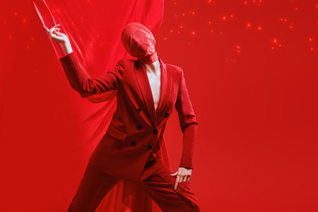 Fashion shoot. Vivid portrait of a high fashion female model in suit and red chiffon fabric on the head posing with expression on red studio background with magic lights.の写真素材