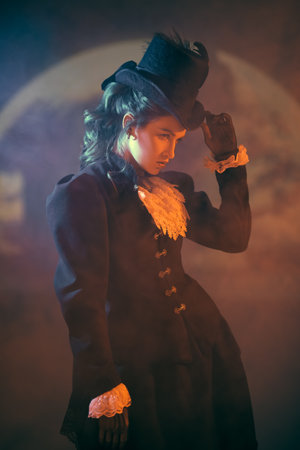 Beautiful young lady in a 19th century suit poses on a dark mysterious background with huge full moon and haze. Vampires. Halloween.の写真素材