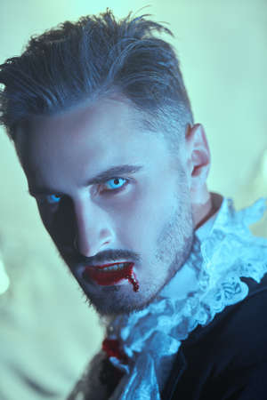 Vampires. Portrait of a handsome vampire man with blood on his lips in an elegant 19th century suit. Halloween.の写真素材