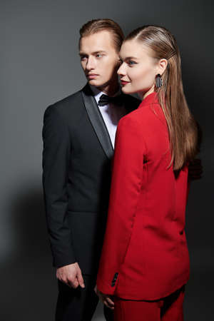 Stunning beautiful young people with elegant hairstyle wearing evening pantsuits pose on a dark gray studio background. Impeccable look. Luxury evening fashion and style.の写真素材