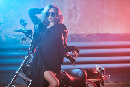 Amazing young woman with wavy blonde hair dressed in a black evening dress and stylish sunglasses...