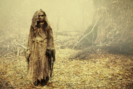 A creepy Scarecrow with a canvas bag on his head, in a burlap robe stands in a dense forest. Vintage style. Halloween Tales. Horror, thriller.の写真素材