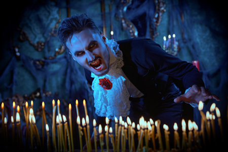 Bloodthirsty vampire with an angry look baring his teeth among burning candles illuminating his dark...