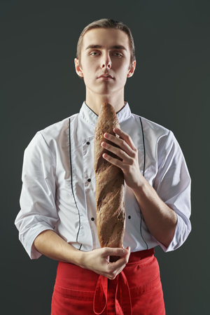Studio portrait of a professional male chef holding a freshly baked baguette. Food and meals.の写真素材