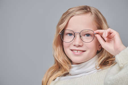 Portrait of an 11 year old girl in a warm sweater and glasses happily smiling on a grey background. Smart schoolgirl in glasses. Close up shot.の写真素材