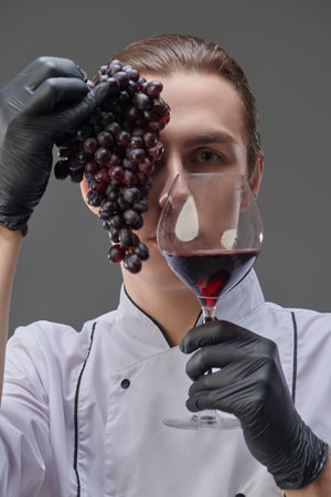 Professional chef in white uniform poses holding a glass of excellent red wine in one hand and a...