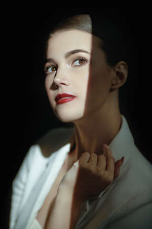 Beautiful young brunette woman with an elegant makeup looks up standing in a beam of light on a black background. Makeup and cosmetics.の写真素材