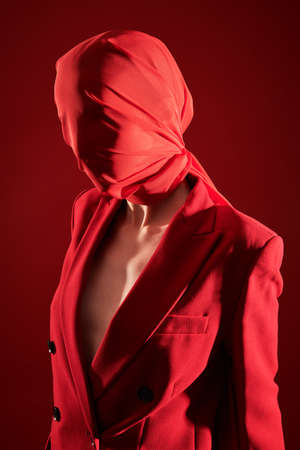 Refined fashion model posing in a smart suit with her face wrapped in red cloth on a red studio background. High fashion and art.の写真素材