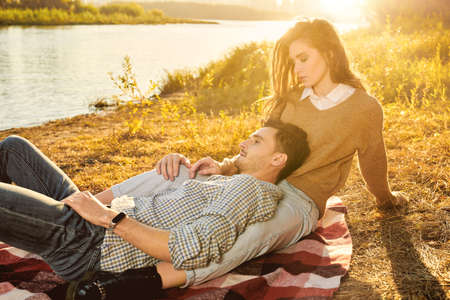 Romantic young couple enjoys a wonderful sunny day having a rest on a blanket by the river. Love concept. Autumn season.の写真素材