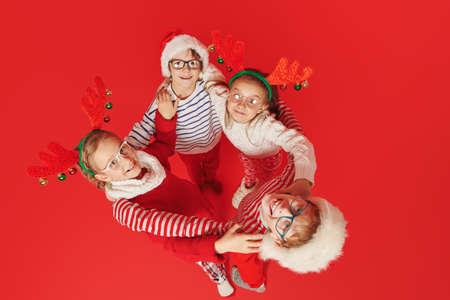 Cheerful kids in Christmas style clothing cheerfully stand in a circle holding each other by the shoulders. Kid's winter fashion. Happy childhood.の写真素材