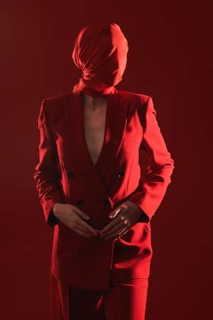 High fashion female model posing in a smart red pantsuit and red chiffon fabric covering her face. Red studio  background. Fashion and red color.の写真素材
