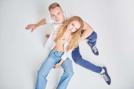 Studio portrait of a beautiful enamored girl and guy sitting next to each other and looking up at the camera. Full length portrait on a white background. Love concept.の写真素材