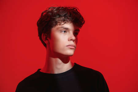 People, emotions. A portrait of a handsome dark-haired guy with a  beam of light on his face looking pensively away. Studio shot on a red background.の写真素材