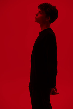 Studio shot in profile of a handsome dark-haired guy standing on a red background holding hands...
