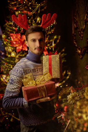 Happy New Year and Merry Christmas! A joyful handsome young man stands with gifts in his hands and...